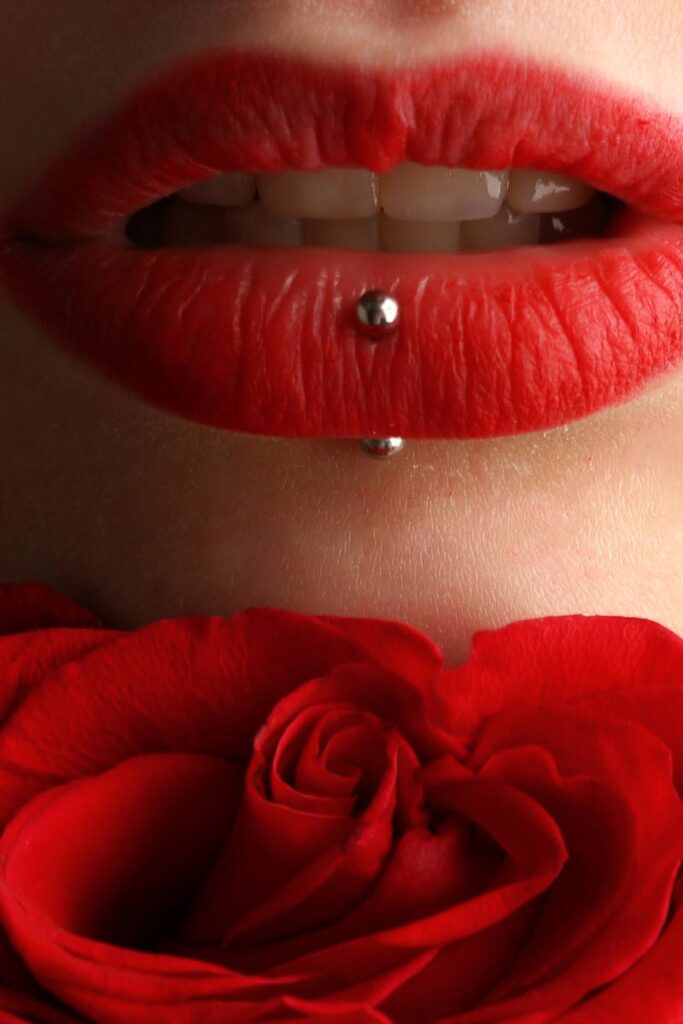 Aesthetic close-up featuring red lipstick, lip piercing, and a red rose.