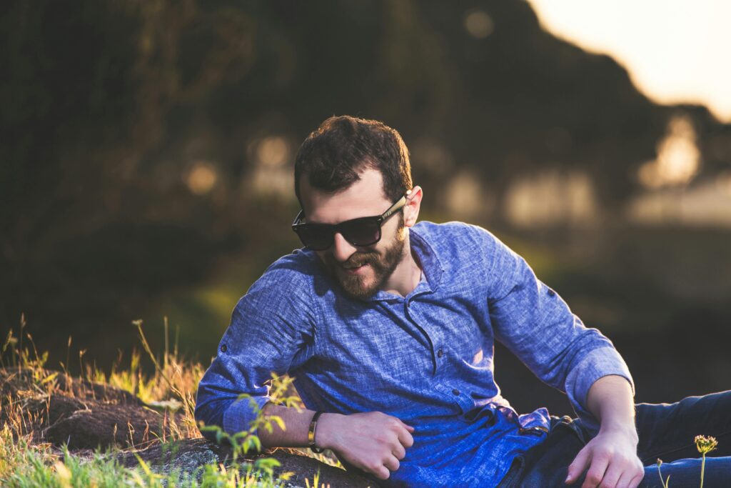A fashionable man with sunglasses lounges outdoors, enjoying a sunny day in nature.